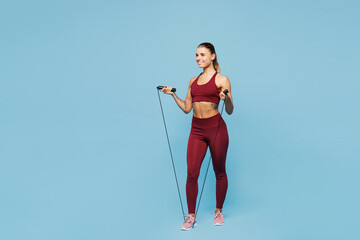 Full body young happy fitness trainer instructor sporty woman sportsman wear red sportswear train in home gym using skipping rope jump isolated on plain blue background. Workout sport fit abs concept.