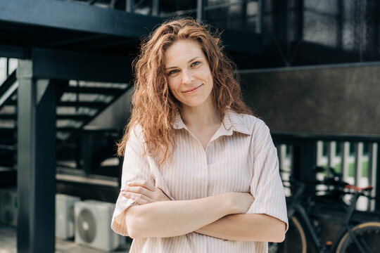 A beautiful confident woman stands with her arms crossed against the background of a modern city building.