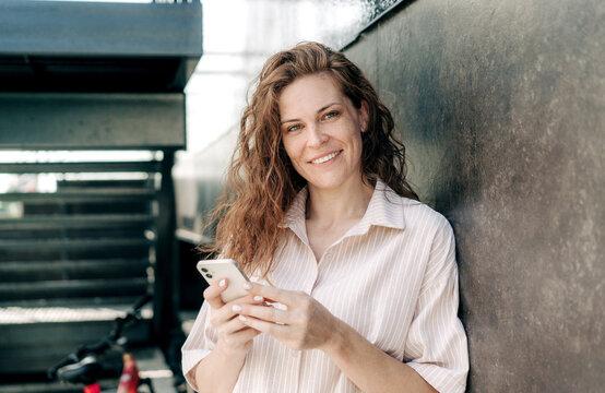 A beautiful red-haired freckled woman is using a mobile phone outside.