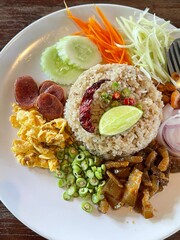 Close up shot of Thai shrimp paste fried rice with shallot, sweet barbeque pork, fried egg, vegetable and spicy chili.
