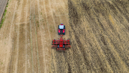 Aerial drone photo of a tractor with a disc harrow cultivating a harvested field, showing parallel...
