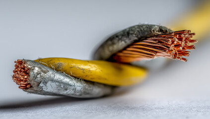 A macro shot of two copper wires, one yellow and the other gray. The connection points of the wires are made of metal, glowing with orange light