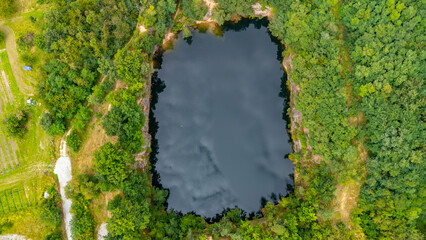 Aerial drone photo of a small forest pond with a dark water surface, surrounded by dense green...