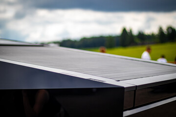 Detailed view of a sleek, angular vehicle roof with reflective panels, set against a blurred outdoor background with greenery and people.