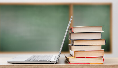 open laptop and stack of books on blackboard background. education concept