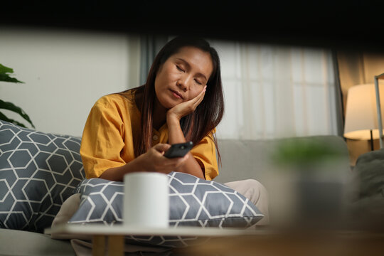 Selective focus shot, Middle-aged Asian woman relaxing on sofa enjoying watching movie alone in living room at home. Relaxing moment.