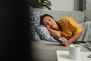 Selective focus shot, Middle-aged Asian woman is lying on a sofa and enjoying watching a movie on television in living room at home. Holiday activities