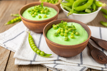 Green pea soup on a wooden table. Fresh pea soup bowl. Delicious healthy cream soup in a bowl with green peas and croutons. Healthy vegan puree. Copy space. Space for text.