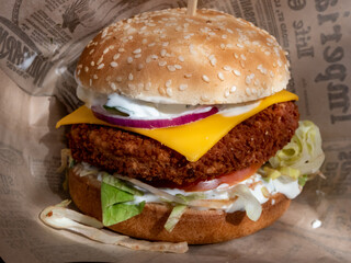 Close-up of a Burger with meat patty, shredded lettuce, tomato, cheese and creamy mayonnaise in toasted bun in a napkin
