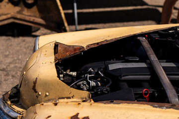Detailed view of a weathered yellow vintage car with a rusty hood, partially revealing the engine components under sunlight.