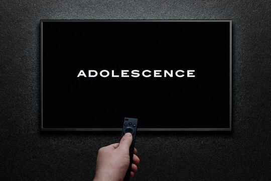 Adolescence TV series trailer or movie on TV screen. Man turns on TV with remote control.