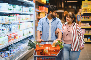 Indian couple choosing food, pushing shopping cart in supermarket