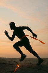 Silhouette of male athlete sprinting at sunset crossing finish line on cracked ground