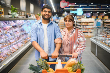 Happy indian couple shopping for groceries in supermarket