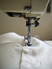 Detailed close up of a vintage sewing machine carrying a soft white fabric.
