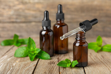 Essential oil mint on a wooden background. Peppermint essential oil with fresh mint leaves. A bottle of aromatherapy oil. Mint extract. The concept of natural cosmetics, spa care. copy space