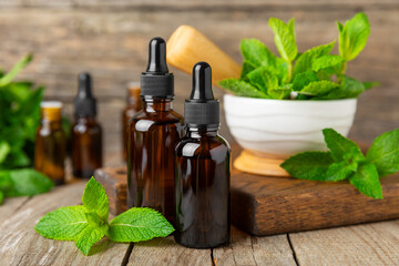 Essential oil mint on a wooden background. Peppermint essential oil with fresh mint leaves. A bottle of aromatherapy oil. Mint extract. The concept of natural cosmetics, spa care. copy space