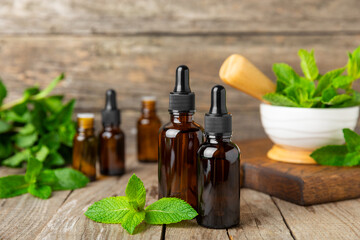 Essential oil mint on a wooden background. Peppermint essential oil with fresh mint leaves. A bottle of aromatherapy oil. Mint extract. The concept of natural cosmetics, spa care. copy space