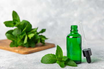 Essential oil mint on a wooden background. Peppermint essential oil with fresh mint leaves. A bottle of aromatherapy oil. Mint extract. The concept of natural cosmetics, spa care. copy space
