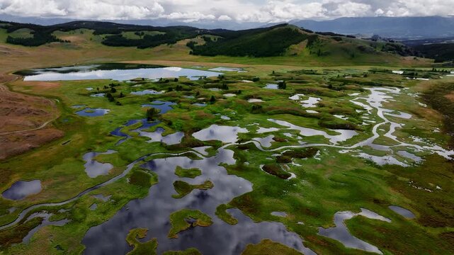 Meandering stream and river against the backdrop of mountains and clouds on the Ukok plateau, Altai Republic. Drone and aerial view. Nature, natural places. Village life.