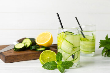 Cucumber water with lemon, lime and mint on a wooden table. Water infused with sliced ​​cucumber in a drinking glass. Tonic refreshing drink. Cucumber lemonade.Summer natural cooling drink.Copy space