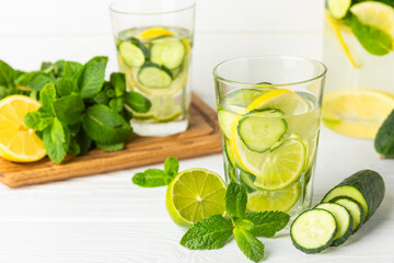 Cucumber water with lemon, lime and mint on a wooden table. Water infused with sliced ​​cucumber in a drinking glass. Tonic refreshing drink. Cucumber lemonade.Summer natural cooling drink.Copy space