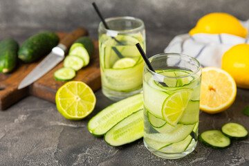 Fototapeta premium Cucumber water with lemon, lime and mint on a wooden table. Water infused with sliced ​​cucumber in a drinking glass. Tonic refreshing drink. Cucumber lemonade.Summer natural cooling drink.Copy space