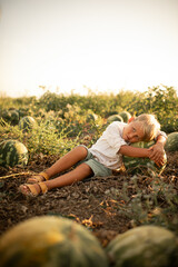 Boy in white shirt sitting on watermelon field, hugging a large ripe watermelon, summer harvest concept, rural lifestyle, fresh organic fruit, countryside farming scene.