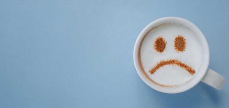 Coffee mug with sad smiley face on blue background, symbolizing Monday blues and low mood