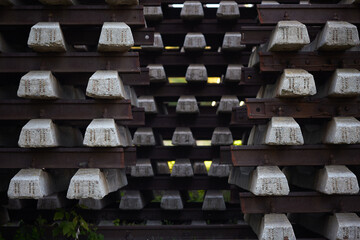 Concrete railway sleepers stacked in multiple layers. Rectangular shapes and rusted metal components. Used in railway construction industry for track stability and alignment. Durable material designed