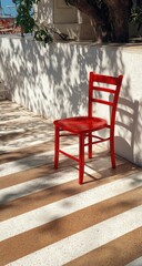 Fototapeta premium Red chair on a striped patio, sunlit shadows