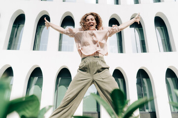 Obraz premium Happy energetic Caucasian woman jumping against the background of a building with arches.