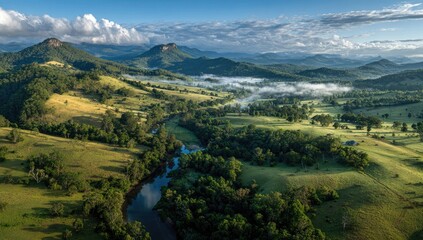 Fototapeta premium High-angle view of rolling hills, valleys, a river winding through lush green foliage, and distant misty mountains under a partly cloudy sky