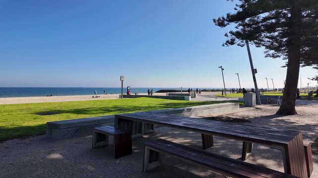 People walking and jogging along grassy foreshore park or coastal trail at Elwood Beach on a sunny day. Concept of Melbourne coastal lifestyle, outdoor recreation and bayside living