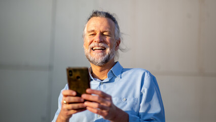 Happy senior man laughing while using smartphone