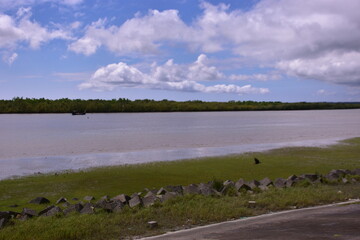 The wide Bakkhali River estuary in Cox's Bazar, viewed from the protective embankment on a dramatic, cloudy day during the monsoon season.