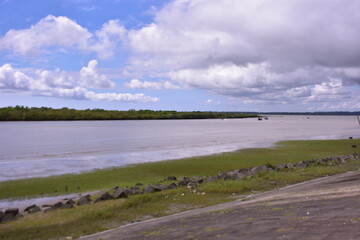 The wide Bakkhali River estuary in Cox's Bazar, viewed from the protective embankment on a dramatic, cloudy day during the monsoon season.