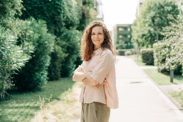 A beautiful woman stands on the territory of a residential complex and looks at the camera smiling.