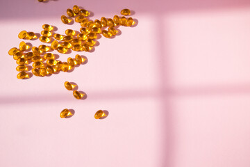Golden capsules scattered on a soft pink surface, illuminated by natural light, creating a warm and inviting atmosphere, ideal for health and wellness themes