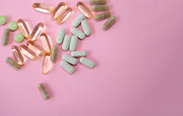 Assorted dietary supplements including capsules and tablets scattered on a pink background, showcasing various shapes and colors for health and wellness concepts