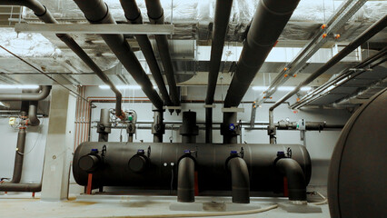 Industrial pipes and valves connecting to a large tank in a boiler room
