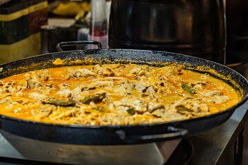 Large pan of simmering chicken curry with vibrant spices and herbs in a commercial kitchen setting