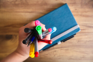 Hand holding colorful pencils on a wooden table, “back to school” themed image. Education, creativity, and school preparation concept.

