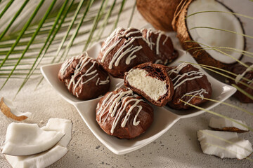 Coconut stuffed chocolate cookies displayed on a plate with coconut pieces and palm leaves in the background