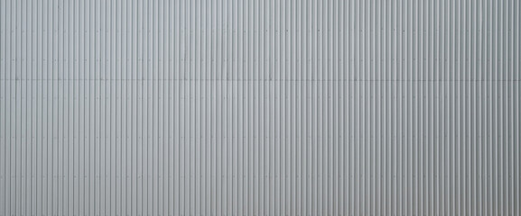 Obraz premium Corrugated metal wall texture with vertical lines reflecting natural light and shadows in an industrial setting
