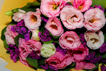 Bright and delicate bouquet of fresh flowers — pink and white lisianthus combined with purple statice, wrapped in yellow craft paper. Close-up, horizontal composition, isolated on a light background. 