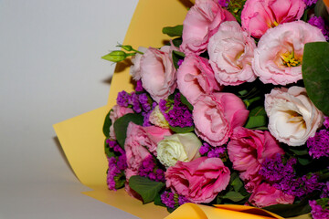 Bright and delicate bouquet of fresh flowers — pink and white lisianthus combined with purple statice, wrapped in yellow craft paper. Close-up, horizontal composition, isolated on a light background. 