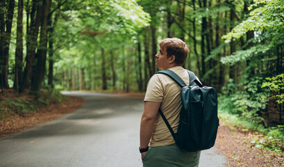 Fototapeta premium One Caucasian male hiking in the woods in summer. Travel, active lifestyle, people and hobby concept. Blonde male in sport clothes standing back outdoors. Traveler enjoys eco-tourism, rear view