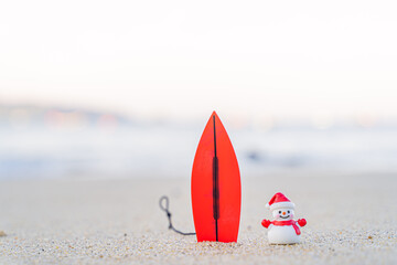 Sandy Christmas Snowman is watching the waves, standing on beautiful beach with a surf board - horizontal version in Patong Beach, Phuket, Thailand