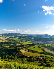 Obraz premium Rolling hills, vineyards, and farmhouses under a vibrant blue sky